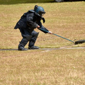 Agente TEDAX con traje antiexplosivos manipulando un artefacto en ejercicio de desactivación de explosivos.